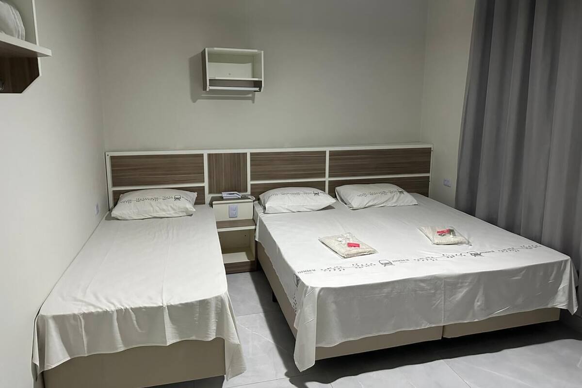 Une chambre double avec deux lits simples, une table de chevet avec une lampe et une petite étagère au-dessus de la tête de lit.