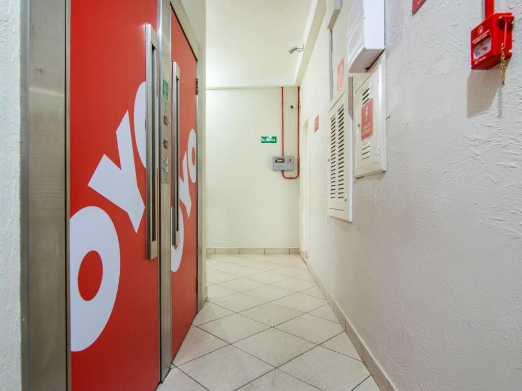 A hallway with a red wall and a sign that reads "OYO". There are fire safety equipment and a control panel on the wall.