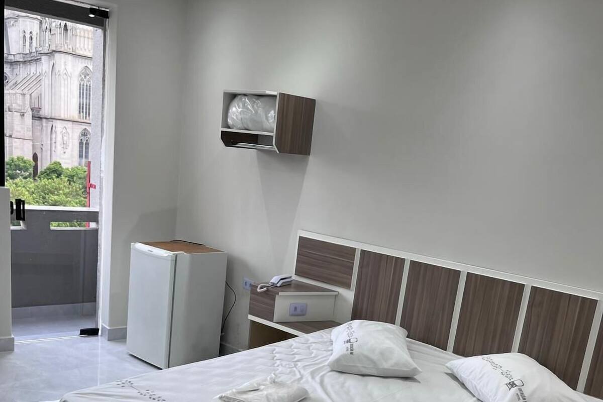 Une chambre d’hôtel moderne dotée d’un grand lit, d’une petite table de chevet, d’un téléviseur intégré et offrant une vue sur un bâtiment historique par la fenêtre.