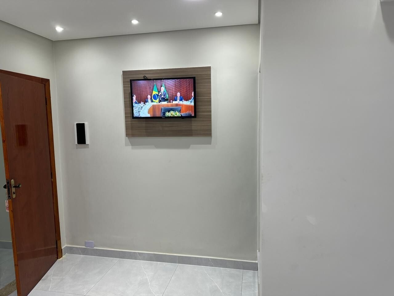 A room with a television mounted on the wall, a wooden door, and tiled flooring.