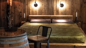 A rustic room with a wooden headboard, a green upholstered bed, a round wooden table, and two black chairs.