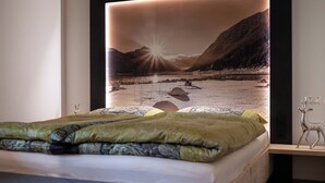 A modern bedroom with a large bed, a wooden headboard, and a wall-mounted artwork of a mountainous landscape.