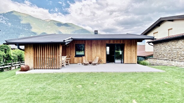 A modern house with a wooden exterior, a patio with two lounge chairs, and a mountain view.