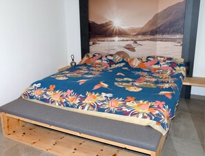 Una cama con una colcha estampada con motivos florales, un cabecero de madera y vistas a montañas a través de una ventana.