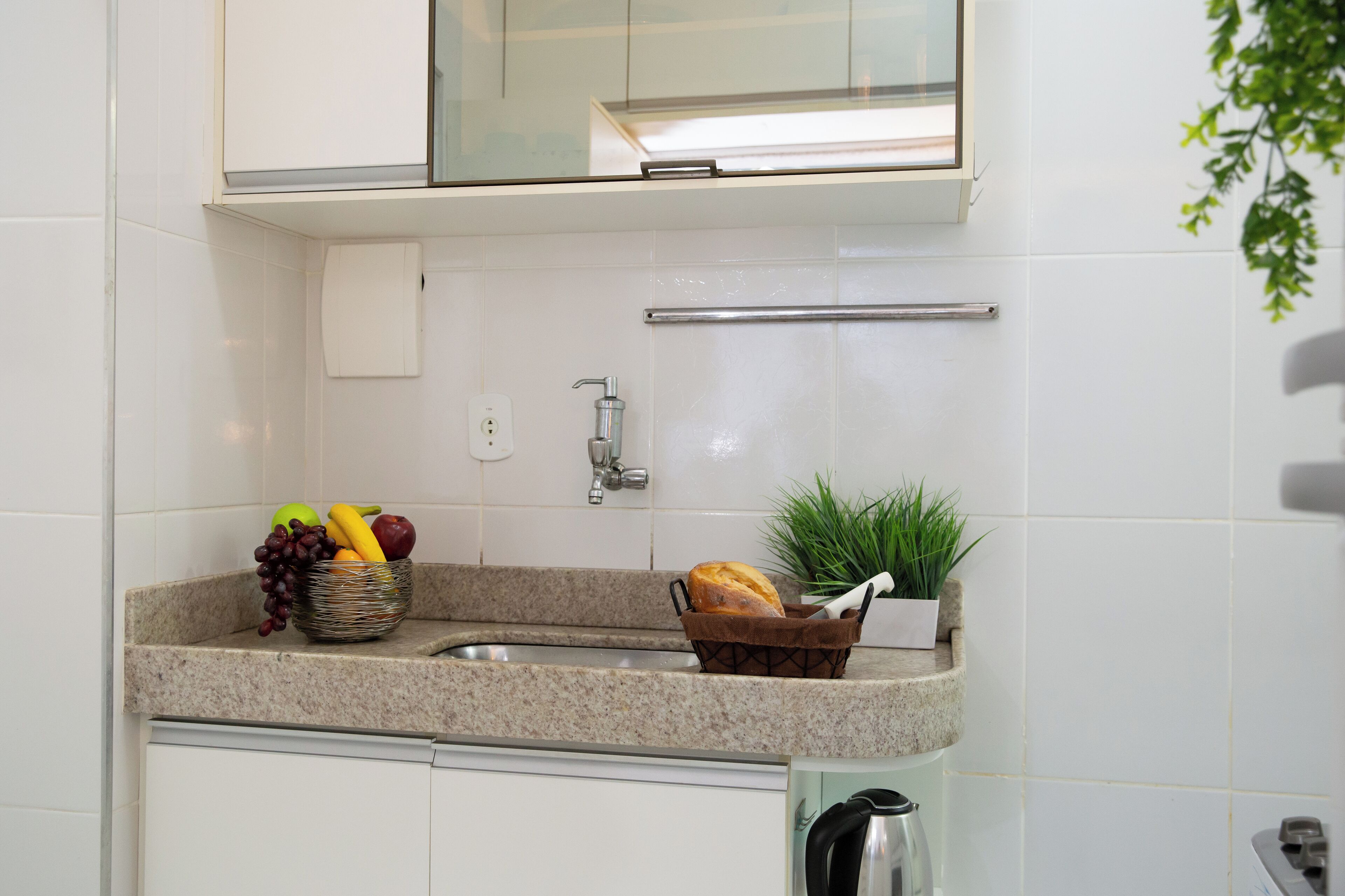 A kitchen with a granite countertop, a sink, a bread basket, a fruit bowl, and a potted plant.