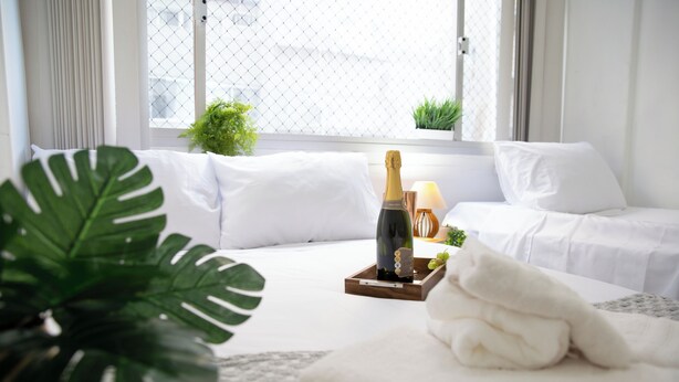 Une chambre d’hôtel bien rangée, avec un lit, une table de chevet sur laquelle se trouve une bouteille de champagne, un plateau avec des verres et une plante en pot.