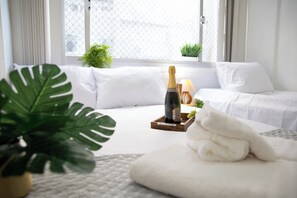 Une chambre d’hôtel bien rangée, avec un lit, une table de chevet sur laquelle se trouve une bouteille de champagne, un plateau avec des verres et une plante en pot.