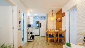Une cuisine compacte dotée d’appareils électroménagers modernes, un coin repas avec des chaises et une table en bois, et un mur en briques blanches.