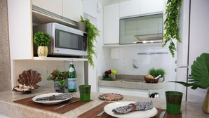 Une cuisine avec des meubles blancs, un four à micro-ondes, un évier et diverses plantes.