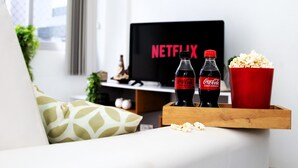 Un salon avec un téléviseur affichant le logo « NETFLIX », deux bouteilles de Coca-Cola, un récipient à pop-corn et un plateau en bois.