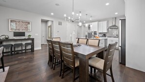 A modern kitchen with white cabinets, a stainless steel refrigerator, and a dining area with a wooden table and chairs. - Pet Friendly New Luxury home on Buffalo Run Golf Course - Pool Table, BBQ (Commerce City)