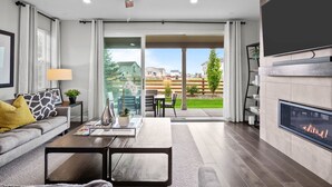 A modern living room with a fireplace, a ceiling fan, and a view of the backyard. - Pet Friendly New Luxury home on Buffalo Run Golf Course - Pool Table, BBQ (Commerce City)