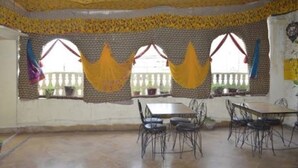 A room with a long table and chairs, large windows with curtains, and a balcony visible through the windows. - Hotel Nutella Jaisalmer By GRB (Jaisalmer)