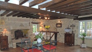 Een rustiek interieur met een stenen openhaard, een houten plafond en een eethoek met metalen stoelen en een glazen tafel.