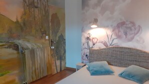 Een slaapkamer met een bed, nachtkastje, muurschildering en lamp.