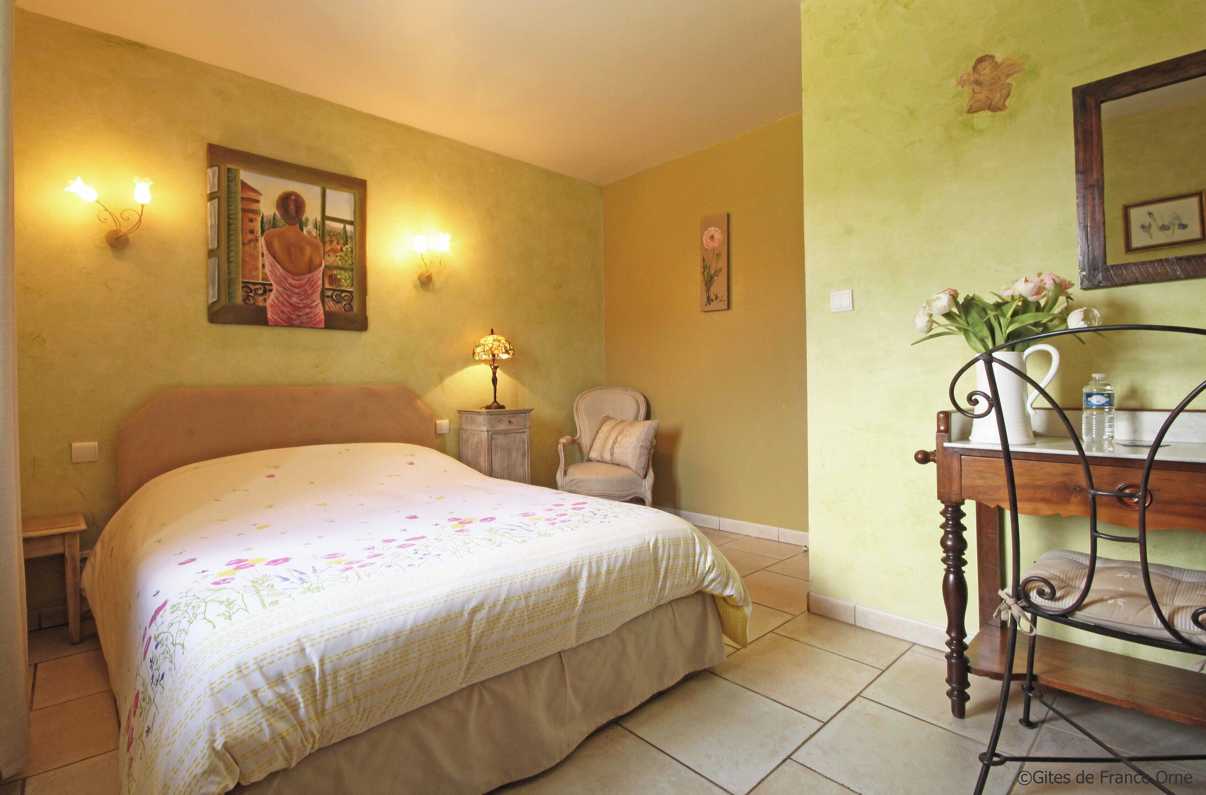 A bedroom with a bed, a chair, a nightstand, a lamp, a mirror, and a dresser.