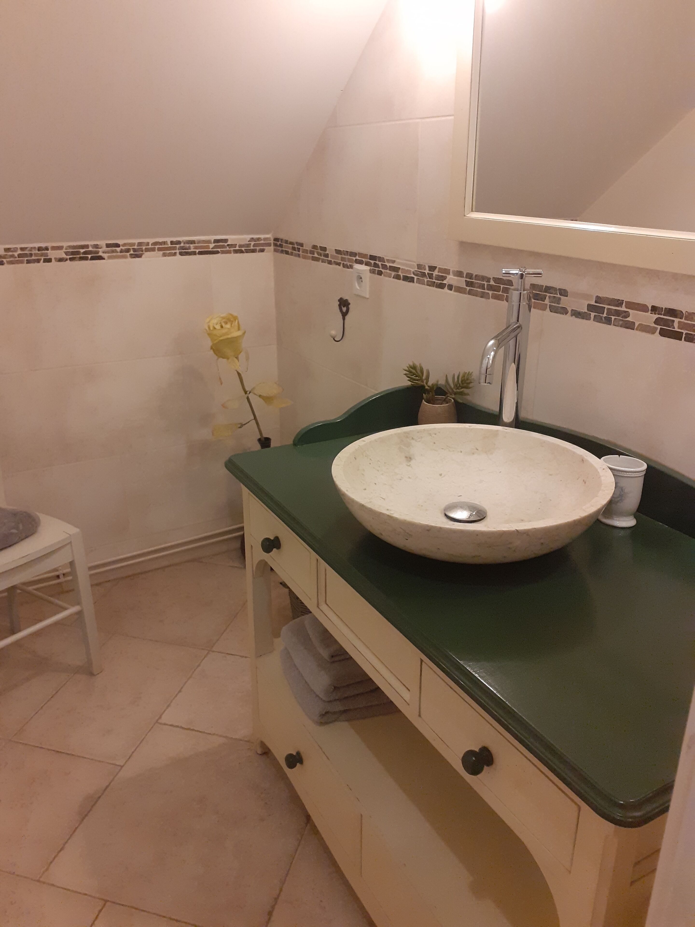 A bathroom with a round sink, green countertop, and a white cabinet with a mirror above it.