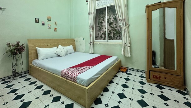 A bedroom with a wooden bed, a mirror, a window with curtains, and a tiled floor. - Hotel O Asti Residence 1 (Surabaya)