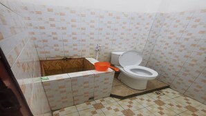 A small bathroom with a toilet, a wooden box, and a plastic basin. - Hotel O Widan Homestay (Samarinda)