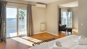 Une chambre d’hôtel avec un lit, une chaise, un radiateur et une vue sur la mer grâce à de grandes fenêtres.