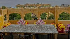 A terrace with a table and chairs, a view of a fort in the background, and a patterned floor.