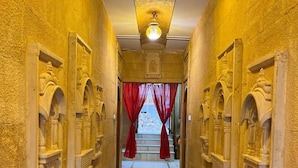 A corridor with marble flooring and ornate wall decorations, leading to a staircase with red curtains.