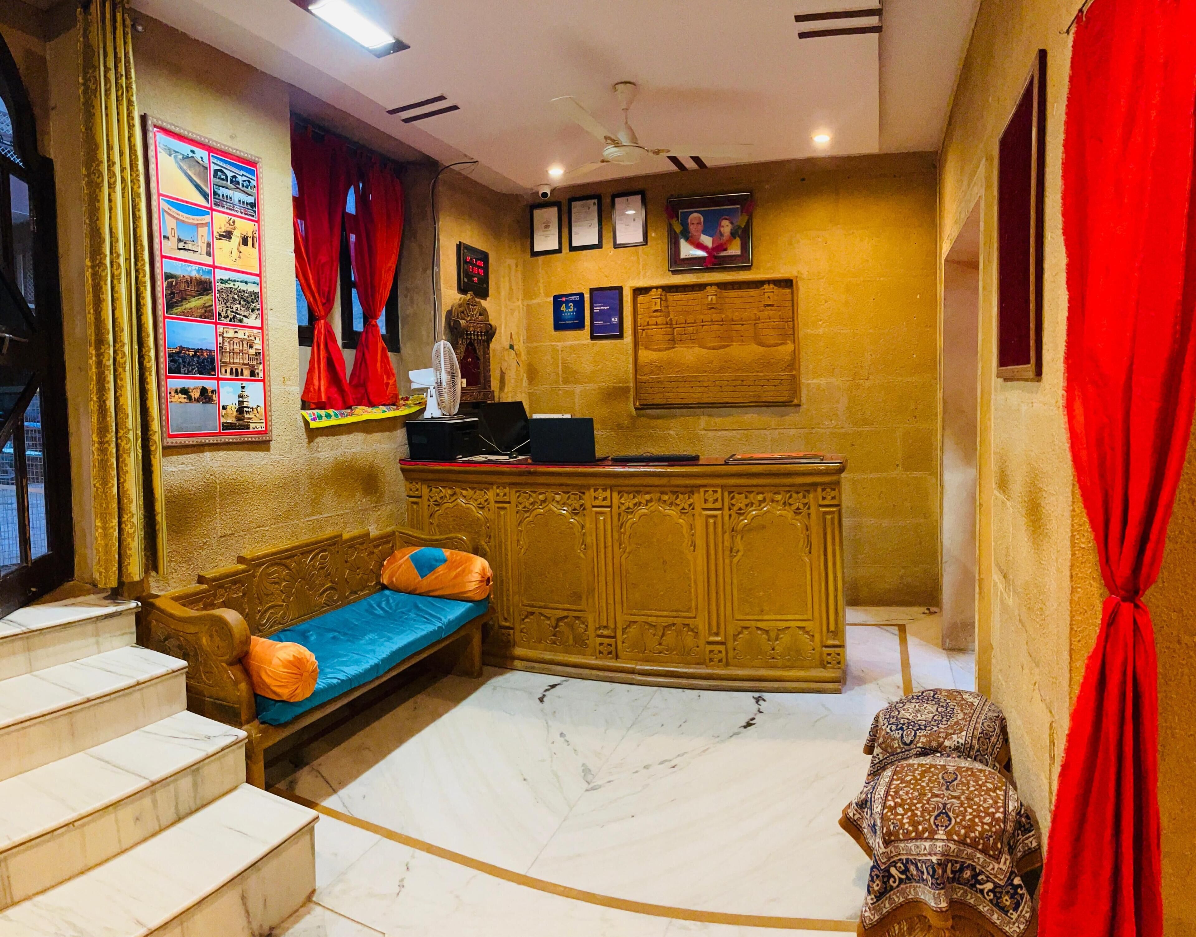 A hotel room with a marble floor, a sofa with cushions, a small bed, a reception desk, and a wall with framed pictures and certificates.
