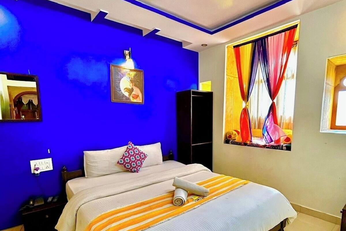 Een slaapkamer met een bed, een plafondventilator, een schilderij en een raam met gordijnen.