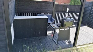 Katettu ulkoalue, jossa on grilli ja tuoli.