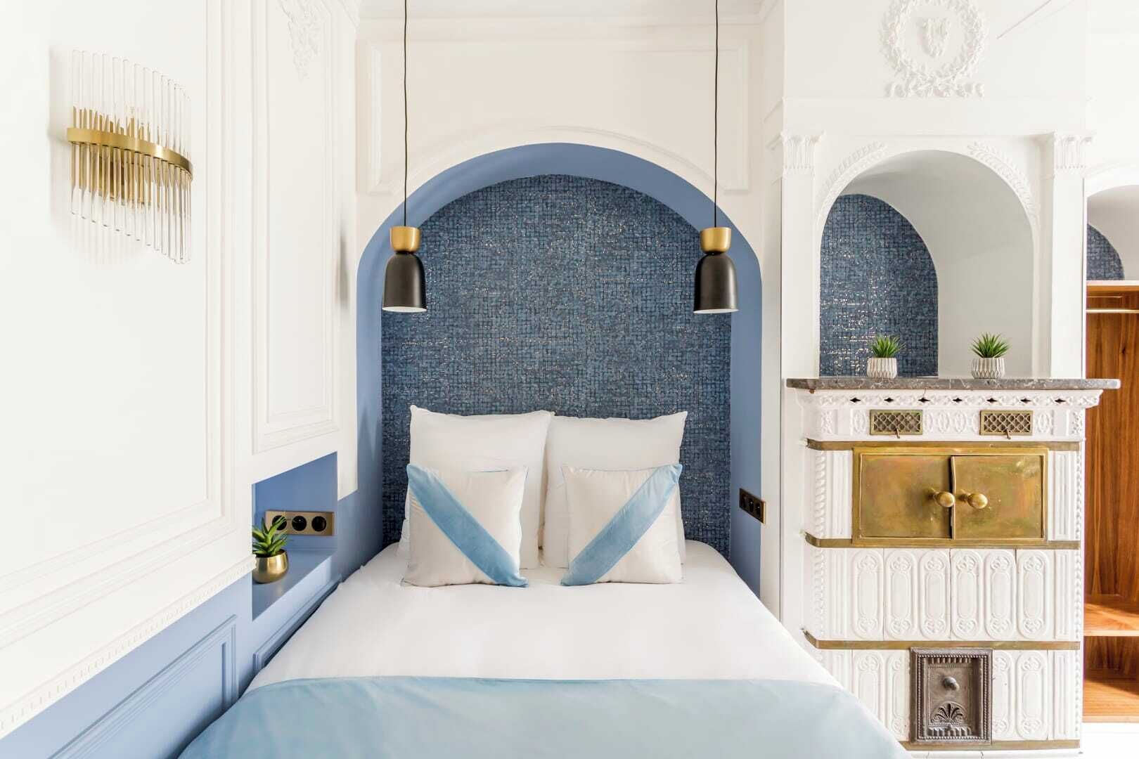 A bedroom with a bed, two hanging lamps, a white cabinet with gold accents, and a blue textured wall.