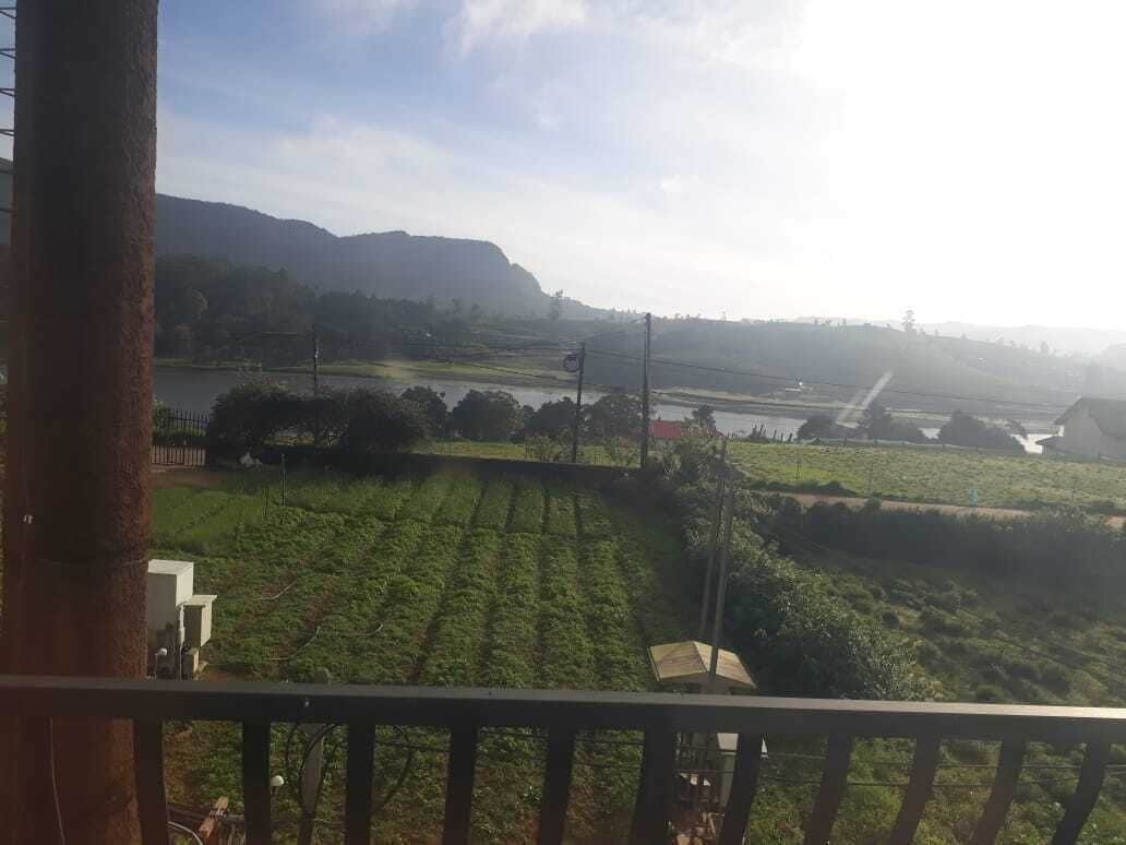 A view from a balcony overlooking a landscape with fields, a river, and distant hills.