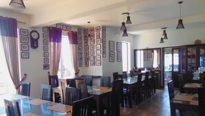 A restaurant with multiple tables and chairs, framed pictures on the walls, and hanging pendant lights.