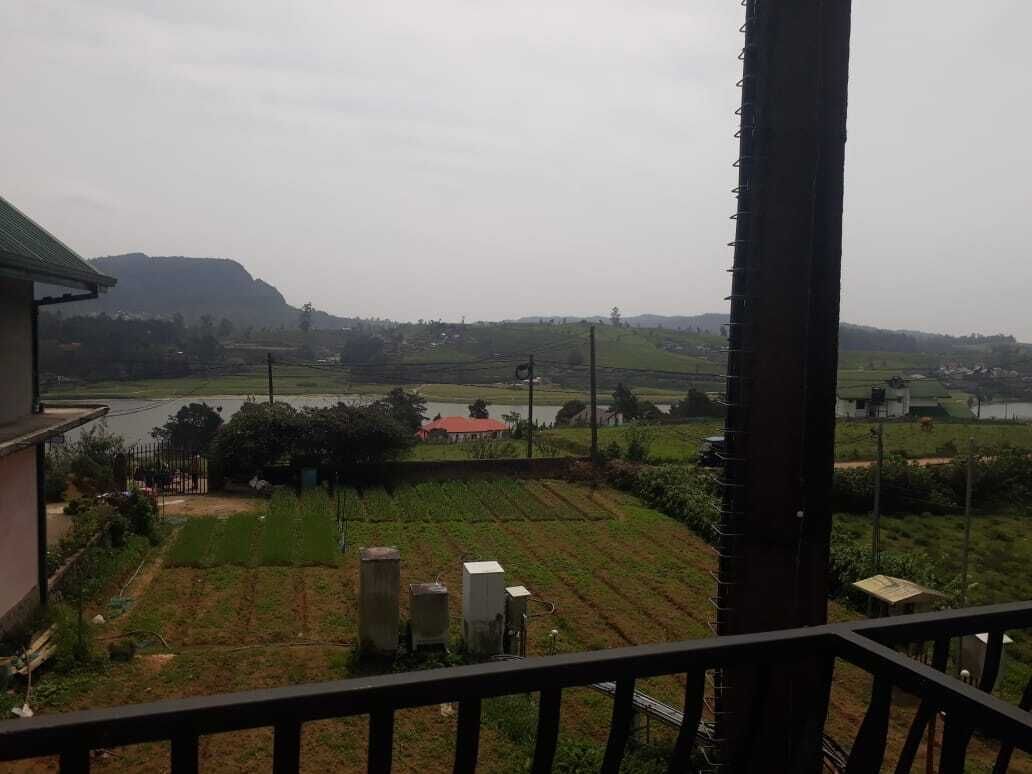 A view from a balcony overlooking a rural landscape with fields, a river, and distant hills.