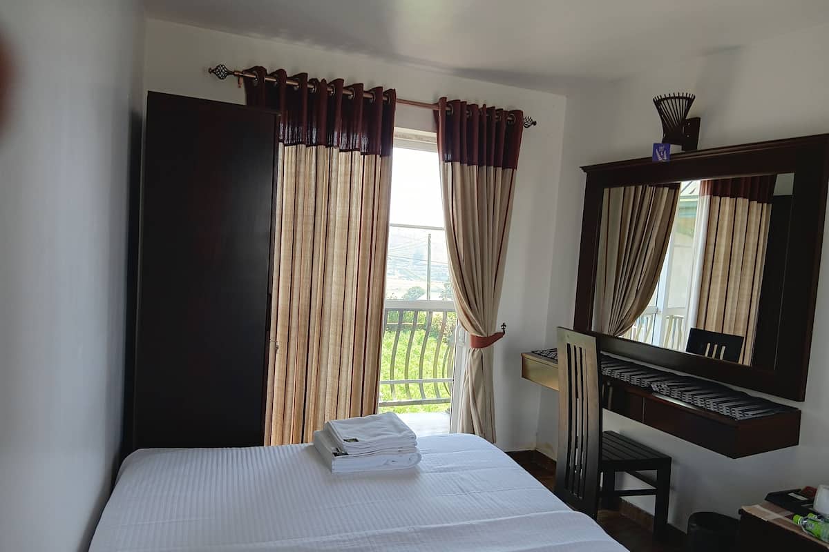 Ein Hotelzimmer mit Bett, Schreibtisch, Stuhl, Spiegel und einem Fenster mit Vorhängen.