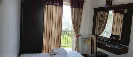 Una camera d'albergo con un letto, una scrivania, una sedia, uno specchio e una finestra con tende.