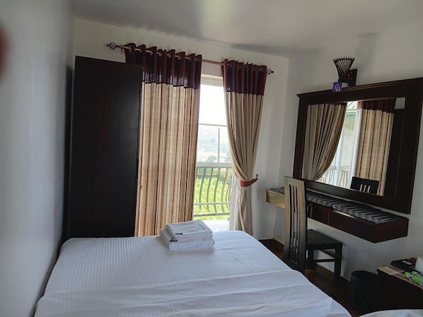 Hotelkamer met een bed, bureau, stoel, spiegel en raam met gordijnen.