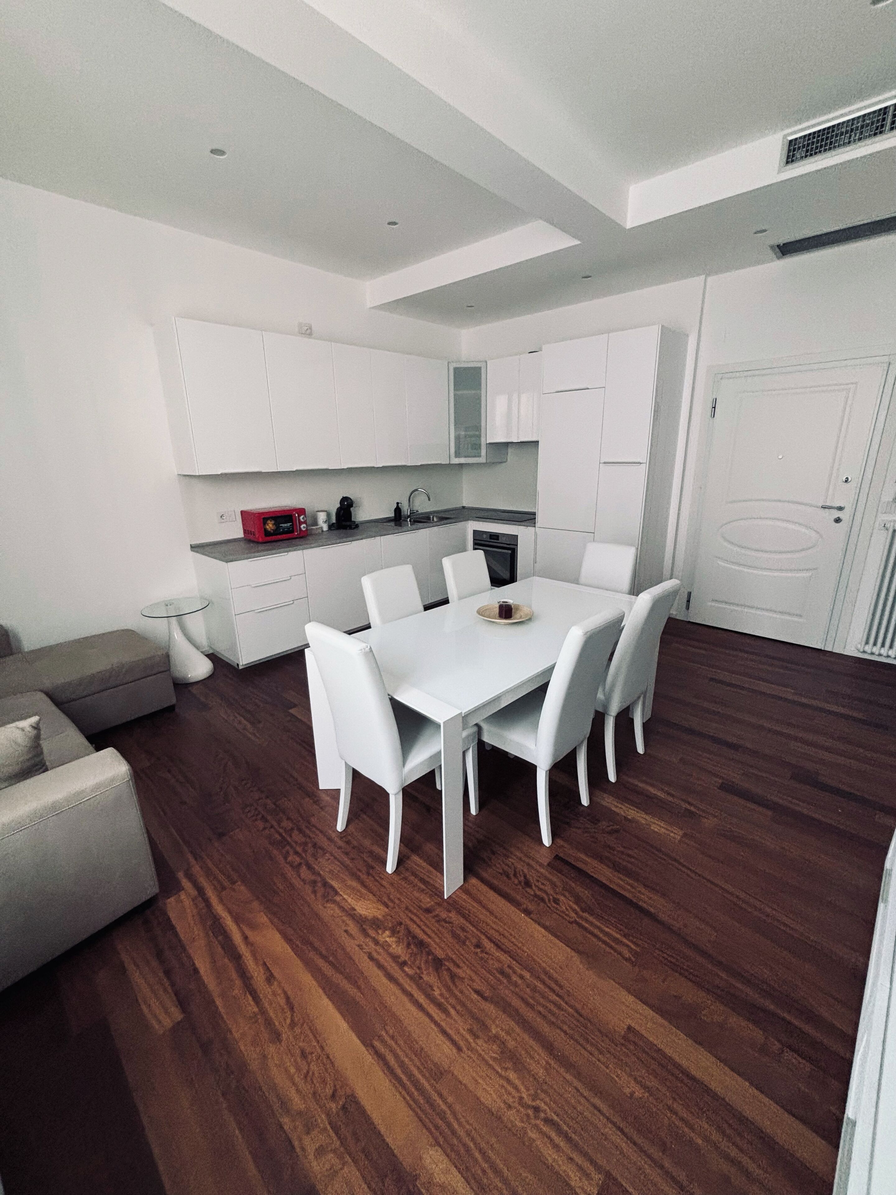 Una cocina moderna con armarios blancos, una mesa de comedor con sillas y un horno empotrado.