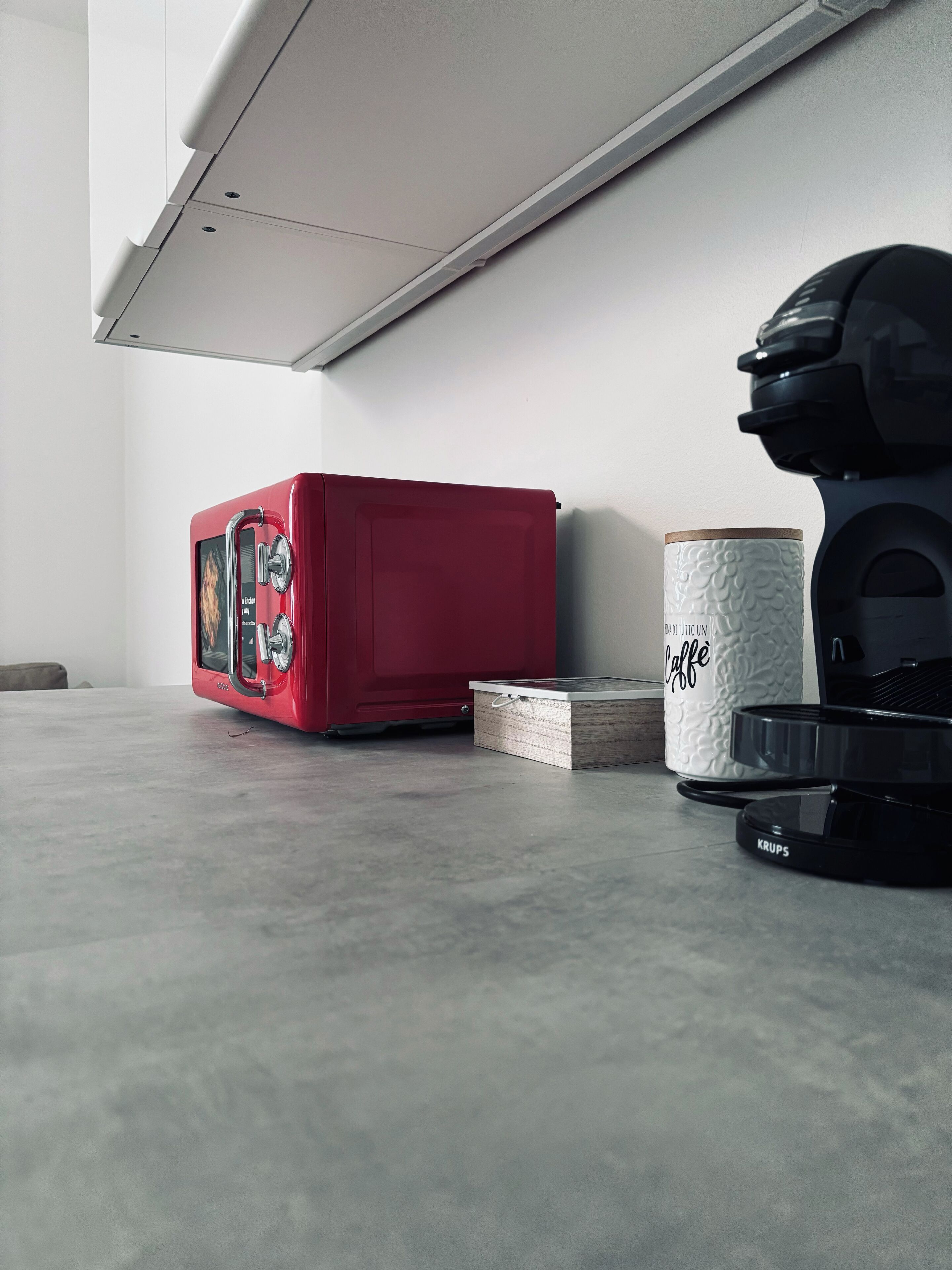 A kitchen with a red microwave, a coffee maker, and a Krups coffee grinder on a countertop.