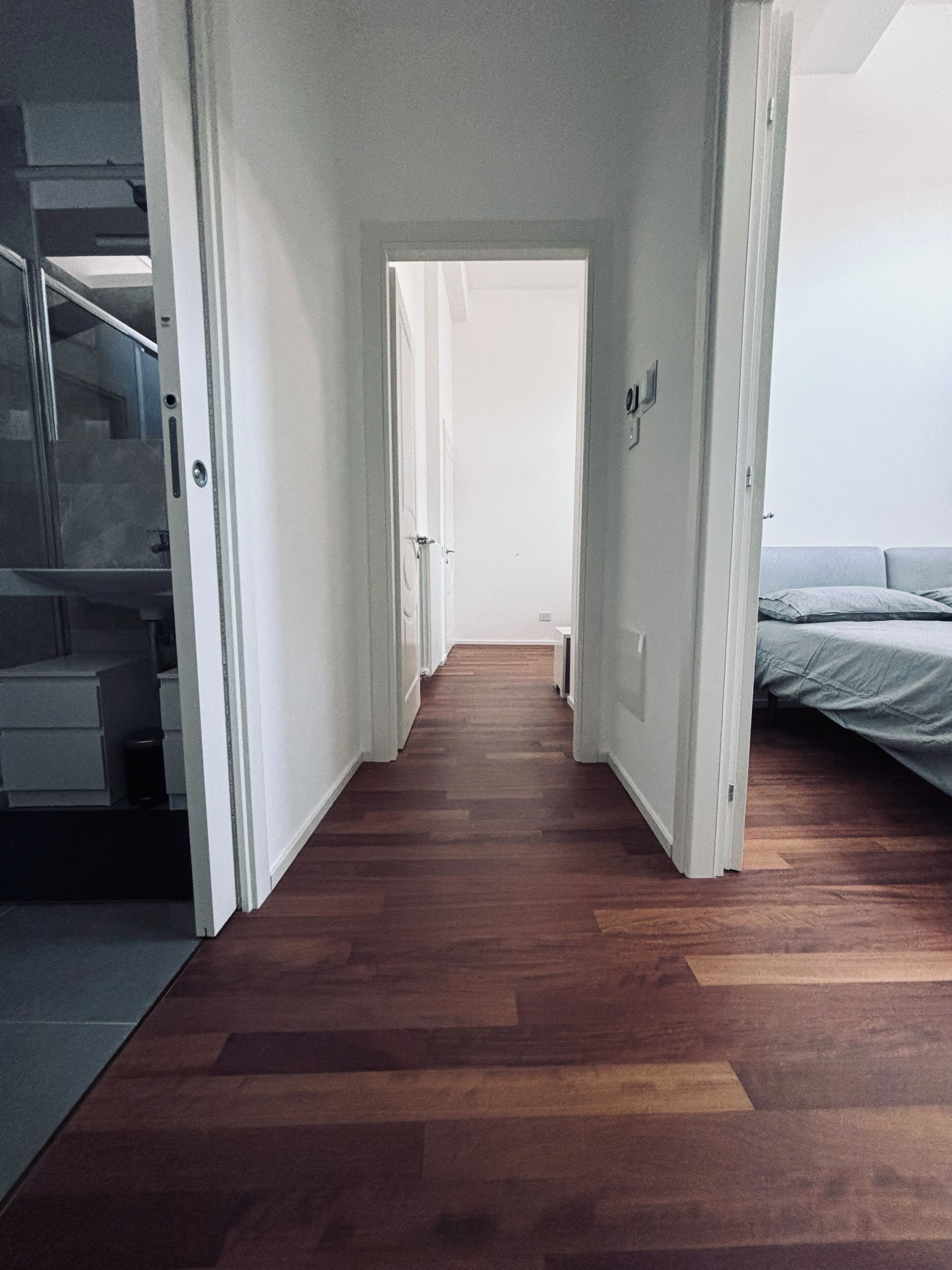 Un estrecho pasillo con suelo de madera que lleva a un dormitorio con cama.