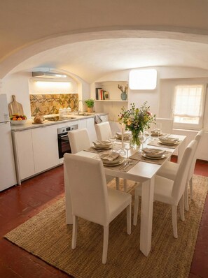 A dining area with a table set for four, white chairs, and a kitchen in the background. - Farini House - apartment in Modena (Modena)