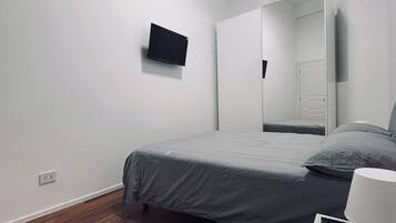 A bedroom with a bed, a bedside table with a lamp, a wall-mounted TV, and a mirror.