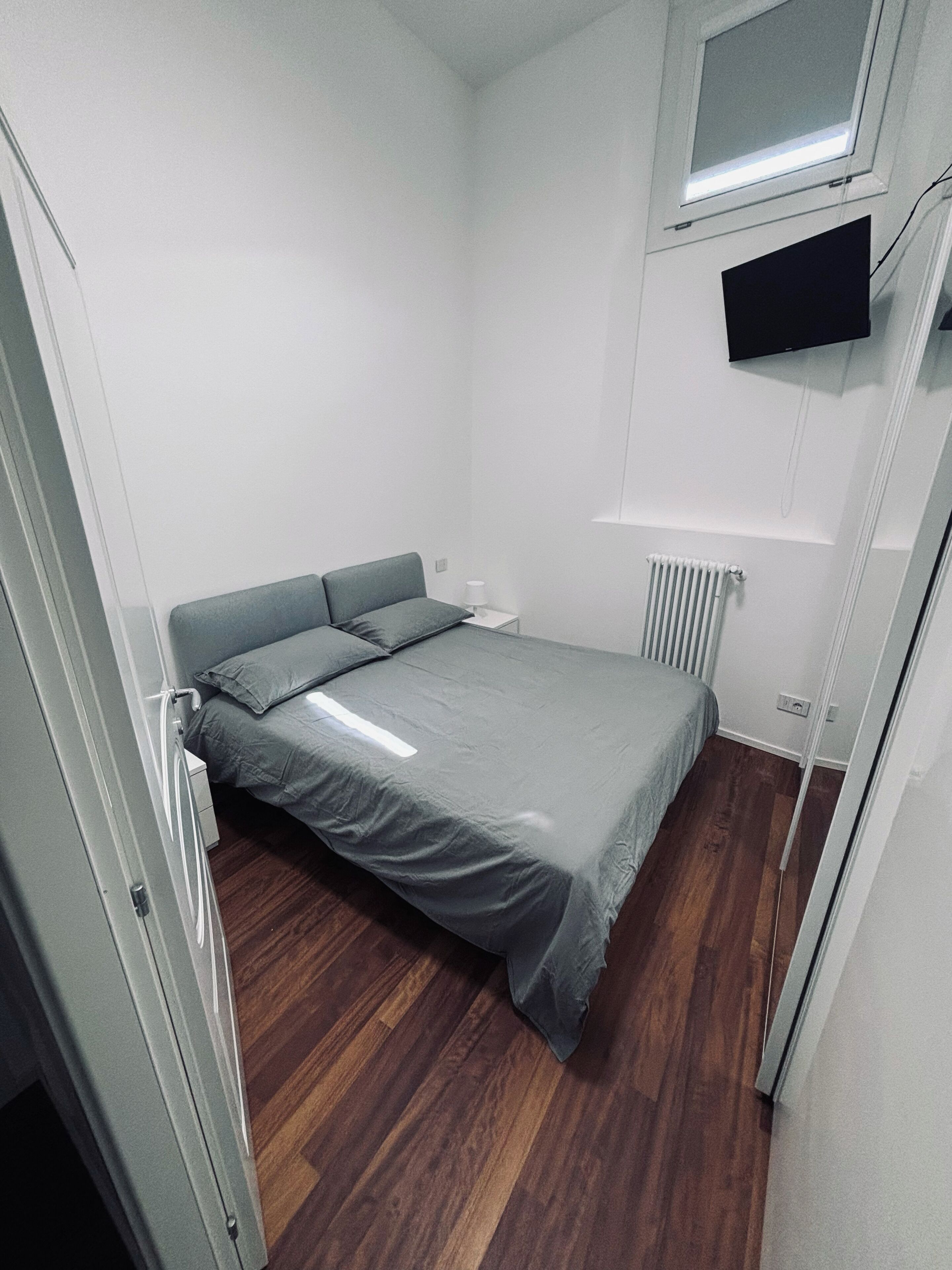 Un dormitorio pequeño y moderno con cama, mesita de noche, televisor montado en la pared y radiador.