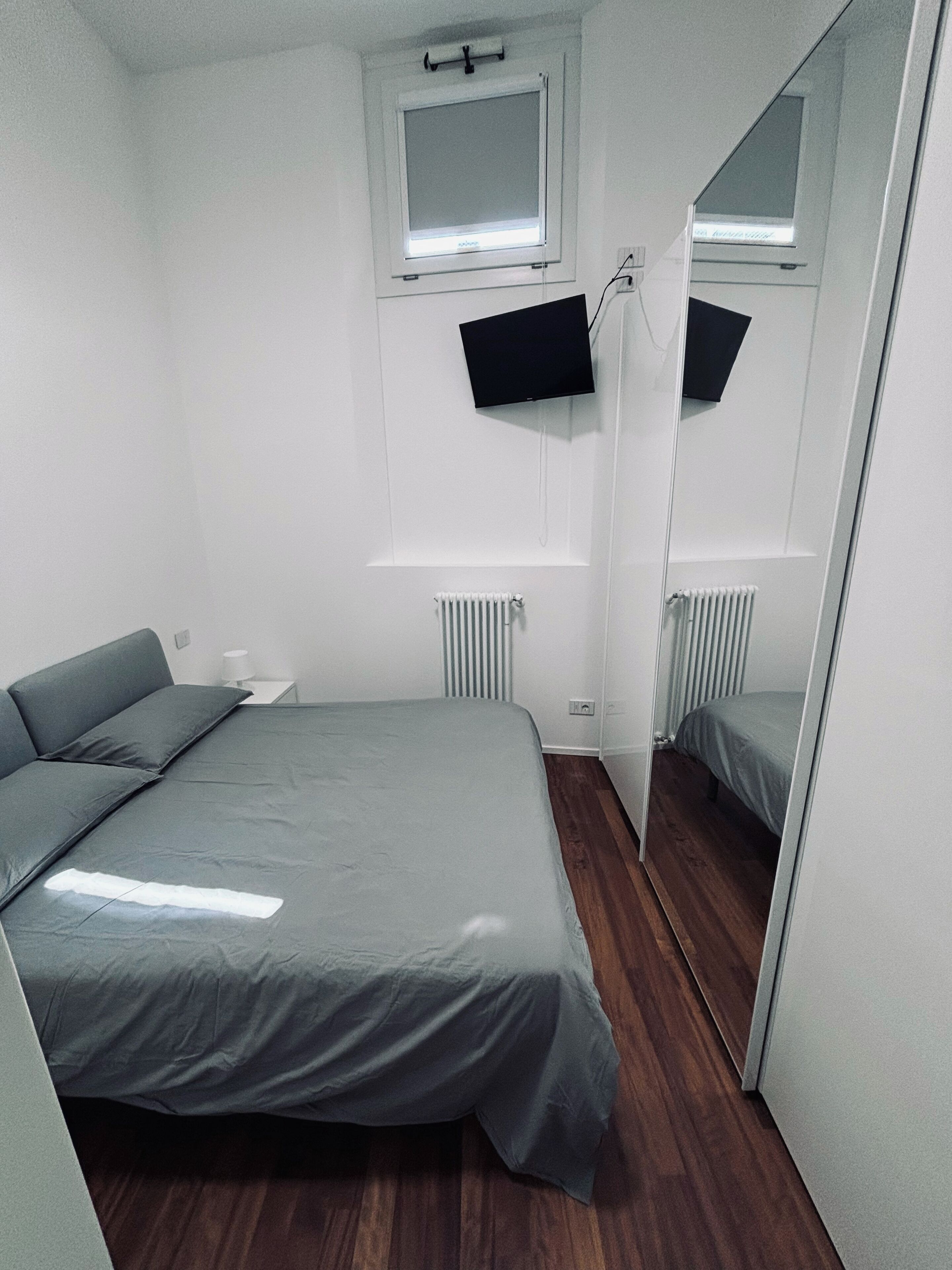 A bedroom with a bed, a window, a radiator, and a mirror.