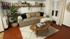 A living room with a sofa, coffee table, and a rug. There are bookshelves with books and plants, and a radiator. - Farini House - apartment in Modena (Modena)