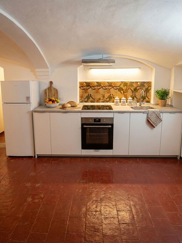 A compact kitchen with white cabinetry, a built-in oven, and a backsplash with a leaf pattern.