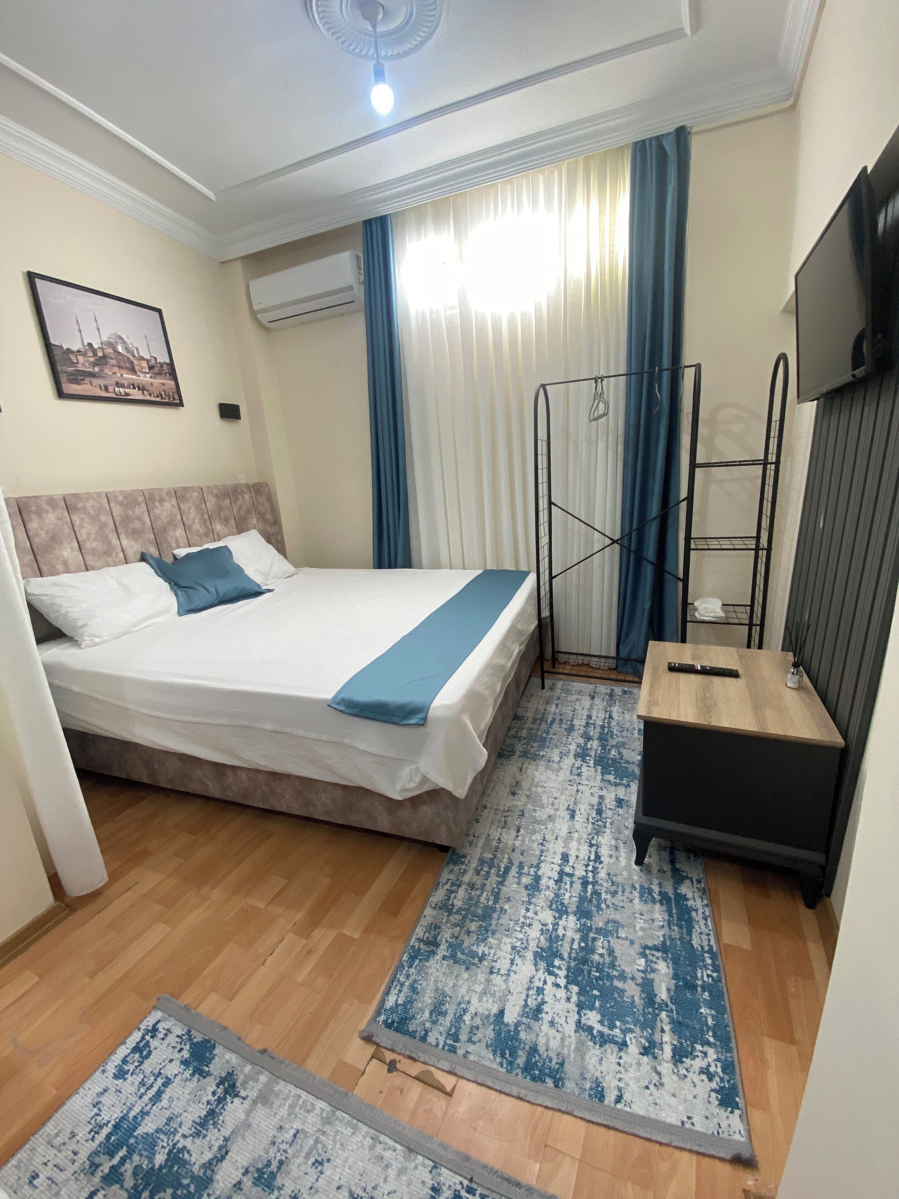 Une chambre d’hôtel équipée d’un lit, d’un bureau, d’une télévision, d’un porte-vêtements et d’une fenêtre avec des rideaux.