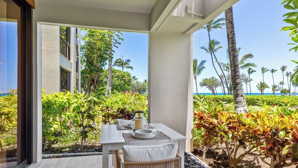 Un coin repas avec une table dressée pour deux personnes, donnant sur un jardin luxuriant et offrant une vue sur la plage.