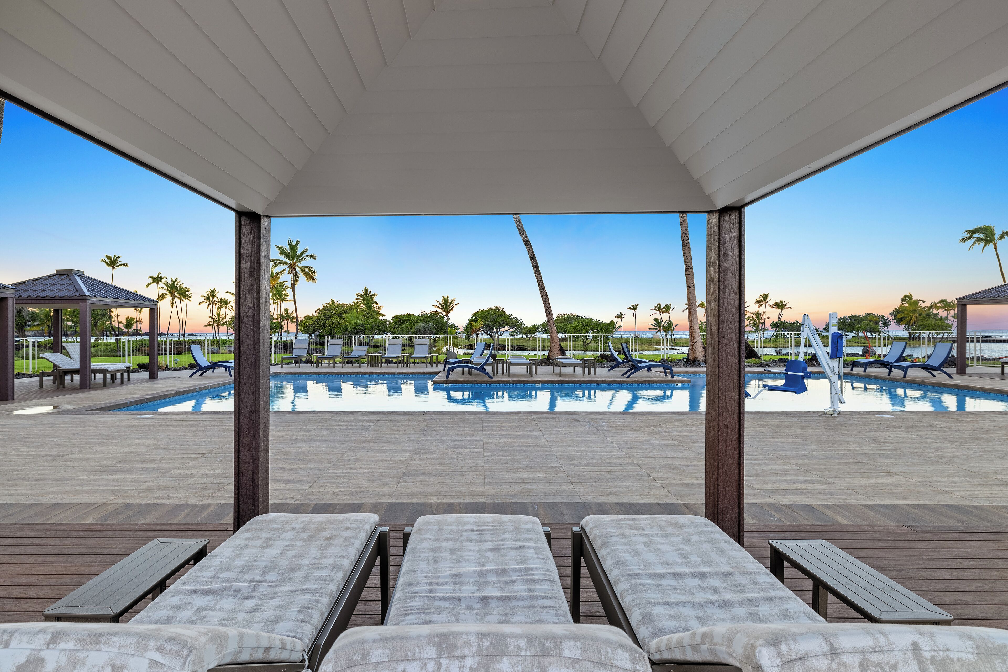 Zona junto a la piscina con sillones de descanso y vistas a la piscina y palmeras.