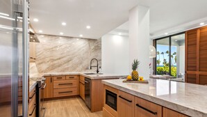 Une cuisine moderne avec des meubles en bois, un pare-feu en marbre et une vue sur l’océan.
