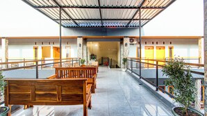 A covered outdoor seating area with wooden benches and potted plants, leading to a building entrance.